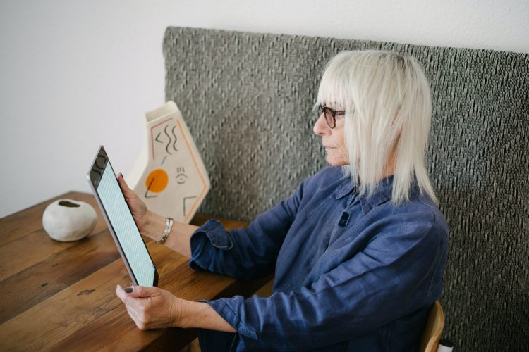 blond-old-woman-reading-book-on-tablet-3867185